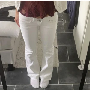 Vita bootcut jeans - Snygga vita bootcut jeans med låg midja och klassisk femficksdesign. Perfekta för en stilren look, dessa jeans har en dragkedja och två knappar framtill.