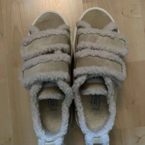 Beige sandaler med pälsdetaljer från Inuikii - Säljer ett par unika beige sandaler från Inuikii med mjuka pälsdetaljer. Perfekta för en mysig look.