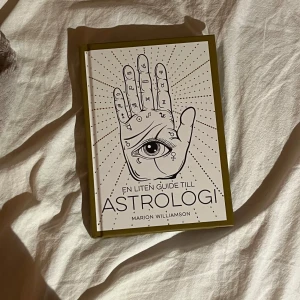 En liten guide till astrologi - Utforska astrologins värld med denna lilla guide av Marion Williamson. Boken har en stilren design med en illustration av en hand och ett öga på omslaget. Perfekt för den som vill förstå stjärntecken och planeternas påverkan.