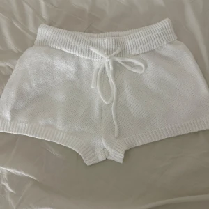 Vita stickade shorts med knytband - Säljer ett par vita stickade shorts med ribbad midja och knytband. Perfekta för en avslappnad look. 