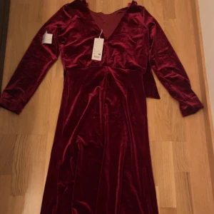 Vinröd sammetsklänning - Elegant vinröd långklänning i mjukt sammetstyg med v-ringning och långa ärmar. Perfekt för högtidliga tillfällen.