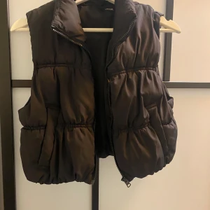 Svart dunväst med dragkedja - Snygg svart dunväst med dragkedja framtill. Perfekt för kyligare dagar och ger en cool look. Västen har en puffig design och är lätt att matcha med olika outfits.