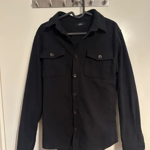 Svart overshirt  - Snygg svart overshirt från Next. Den har inga defekter och är i toppen skick!                                       Hör av er vid eventuella frågor!
