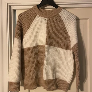Beige och vit stickad tröja från MNG - Säljer en snygg stickad tröja från MNG i beige och vitt. Tröjan har ett unikt blockmönster och långa ärmar med ribbade muddar. Perfekt för kyliga dagar!