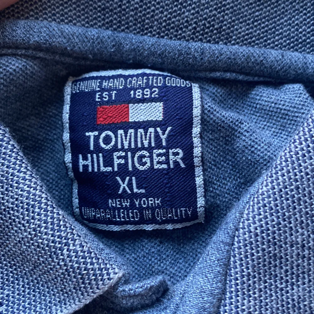 Snygg grå pikétröja från Tommy Hilfiger i storlek XL. Tröjan har en klassisk krage med knappar och det ikoniska logotypmärket på bröstet. Perfekt för en stilren och avslappnad look.. Neuletakit & Villapaidat.