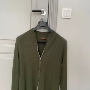 Olivgrön stickad kofta från Stenströms - Säljer en olivgrön stickad kofta från Stenströms med dragkedja framtill. Koftan har en ribbad krage och långa ärmar, perfekt för kyligare dagar. Tröjan är i superbra skicka overall men tyvärr har de kommit ett hål i vänstra armen, dock syns det inte mycket men bör vetas om man köper den. Tveka inte att skriv om de finns frågor😀