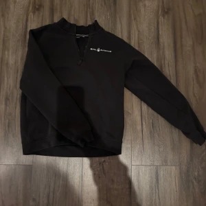 Svart tröja från Sail Racing - Snygg svart tröja från Sail Racing med dragkedja och logotyp på bröstet. Perfekt för en stilren look. Tröjan har långa ärmar och en bekväm passform.