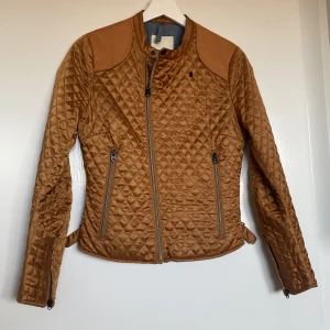 Brun quiltad jacka från G-Star RAW - Säljer en snygg brun quiltad jacka från G-Star RAW i storlek S. Jackan har en cool design med dragkedja och justerbara spännen i midjan. Perfekt för höst och vår med sin stilrena look och bekväma passform. Passar både till vardags och lite finare tillfällen.
