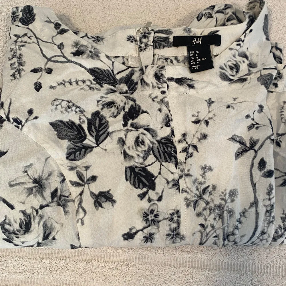 Säljer en superfin vit klänning från H&M med svart blommönster. Den har korta ärmar och en dragkedja i ryggen. Perfekt för sommarens fester eller en mysig vårdag. Klänningen är i nyskick och har en normal passform. 🌸. Klänningar.