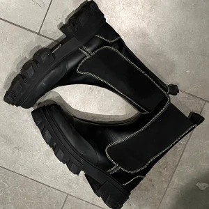 GANNI Mid Chelsea Boots - Säljer ett par GANNI Mid Chelsea Boots åt min sambo. Skorna är nästan helt oanvända, har använts utomhus en gång. Svarta med gul söm.