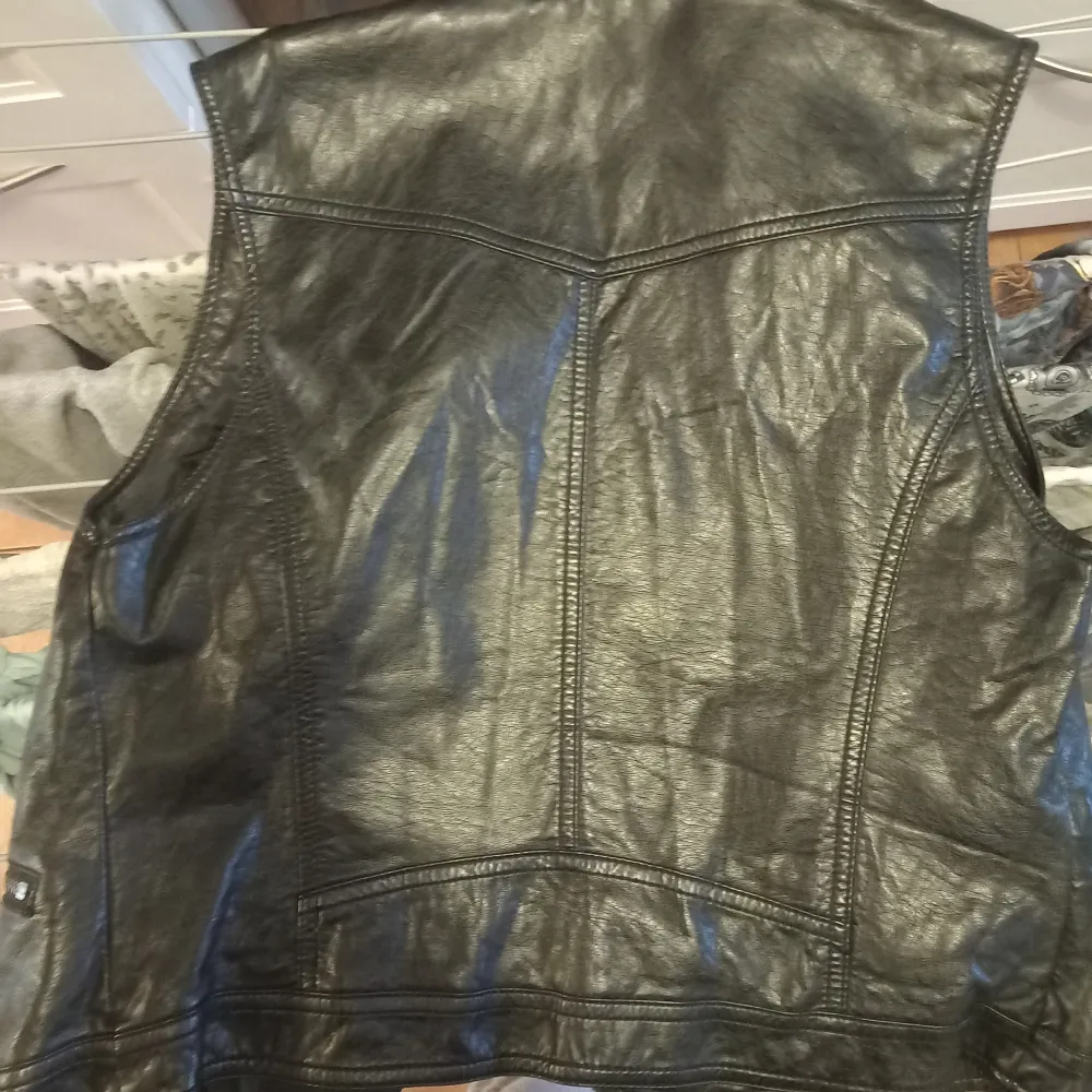 Snygg svart väst i imitation skinn från h&mdivided. Den har en cool bikerstil med flera dragkedjor och en asymmetrisk design. Perfekt för att ge din outfit en edgy touch. Storlek 40, vilket motsvarar dam L. Tillverkad i Kina.. Övrigt.