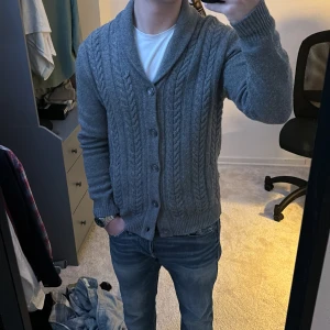 Grå stickad kofta med knappar - Säljer en snygg grå stickad kofta med knappar framtill. Den har ett klassiskt flätmönster och en mysig krage. Perfekt för kyliga höst- och vinterdagar. Passar både till vardags och lite finare tillfällen. 🧥