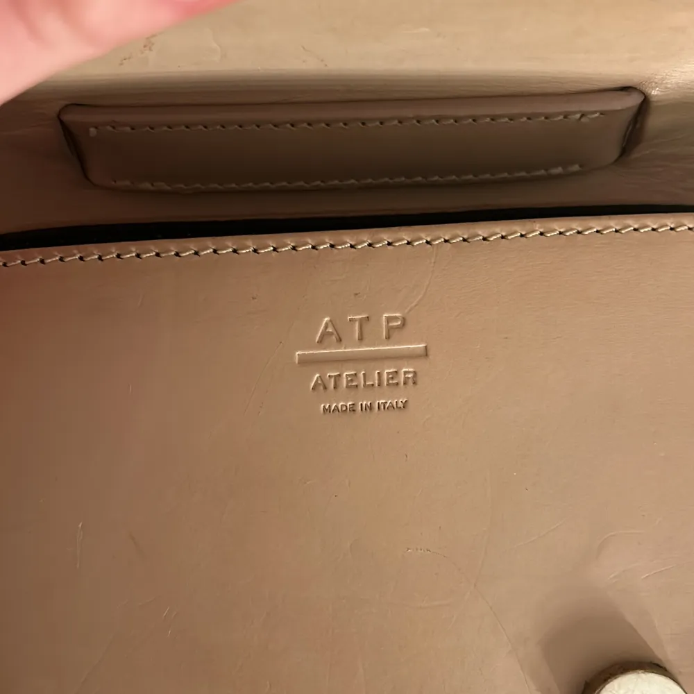 Säljer en stilren beige handväska från ATP Atelier i skinn. Väskan har en elegant design med ett lock. Perfekt för både vardag och festliga tillfällen. Tillverkad i Italien, vilket garanterar hög kvalitet och stil. Passa på att köpa denna snygga accessoar!. Väskor.