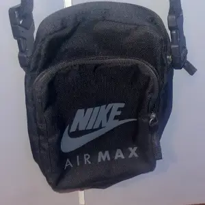 Säljer en svart axelväska från Nike Air Max. Perfekt för att bära med sig det nödvändigaste. Väskan har en justerbar rem och en praktisk dragkedja framtill. Den är stilren och passar till alla tillfällen. Perfekt för vardagsbruk eller när du är på språng!