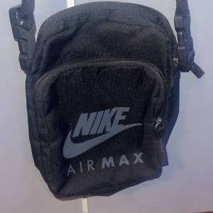 Svart axelväska från Nike Air Max - Säljer en svart axelväska från Nike Air Max. Perfekt för att bära med sig det nödvändigaste. Väskan har en justerbar rem och en praktisk dragkedja framtill. Den är stilren och passar till alla tillfällen. Perfekt för vardagsbruk eller när du är på språng!