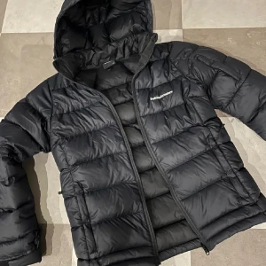 Svart dunjacka från Peak Performance - Säljer en svart dunjacka från Peak Performance i mycket bra skick. Jackan har en dragkedja framtill och en mysig huva. Perfekt för kalla vinterdagar och håller dig varm och bekväm. Passar både till vardags och utomhusaktiviteter.