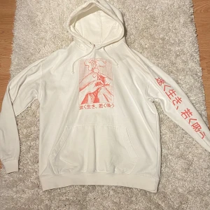 Vit Erick Khan Hoodie - Säljer en vit Erick Khan hoodie med en cool röd grafik på framsidan och text på ärmen. Den har en stor ficka fram och justerbar huva. Perfekt för en avslappnad stil och att hålla sig varm under kyliga dagar. Passar bra till jeans eller joggers!