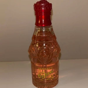 Versace parfymflaska - Säljer en elegant parfymflaska från Versace i en vacker rosa nyans. Flaskan har en unik form med detaljerade mönster och ett rött lock. Perfekt för den som vill ha en lyxig touch på sin parfymkollektion.