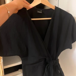 Svart omlottklänning från Stradivarius - Säljer en elegant svart blus från Gina tricot. Blusen har korta ärmar. 