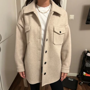 Beige kappa  - Säljer en superfin beige kappa i nytt skick. Den har långa ärmar och stora fickor fram. Perfekt för höst och vår! Den har knappar och ett bälte i midjan för en snygg passform. Passar både till vardags och lite finare tillfällen.