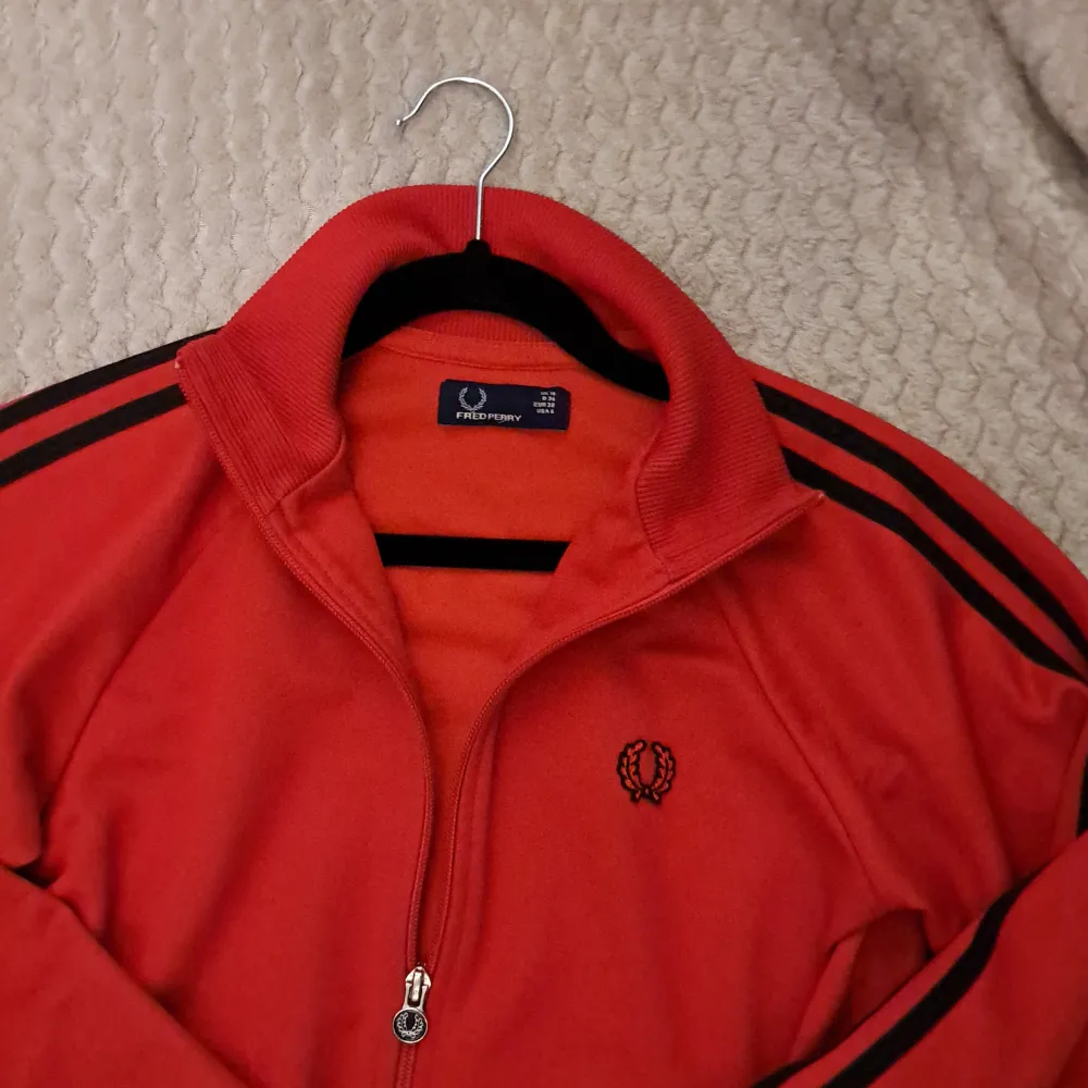 Säljer en snygg röd track jacket från Fred Perry. 🤘💯Den har svarta ränder längs ärmarna och en dragkedja med Fred Perry-logga. Perfekt för höst och vår, med en sportig och retro stil. Jackan är i mycket bra skick och passar perfekt för både träning och vardag. 👍🏼 ny pris 1500. Jackor.