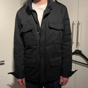 Svart jacka från Zadig & Voltaire - Säljer en snygg svart jacka från Zadig & Voltaire. Den har en cool militärinspirerad stil med flera fickor och dragkedja samt lite slitningar som är använd fåtal gånger. Skön päls i ryggen vilket gör det perfekt till hösten/ vintern! Nypris ligger på runt 5000kr men säljer den för 2199kr! Priset är dock diskuterbart. Tags och annat skoj följer också med! Personen på bilden är 183 cm