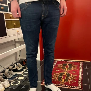 Mörkblå jeans - Säljer ett par mörkblå nudie jeans i bra skick. De har en slim fit. Klassisk design med fem fickor och knappgylf. Passar till det mesta och är superbekväma! Byxorna är näst intill nyskick och är i modellen tight terry storlek 32/30 personen på bilden är 183cm