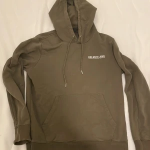 Grön hoodie från Helmut Lang - Säljer en snygg beige hoodie från Helmut Lang, perfekt för höst och vinter. Den har en klassisk design med en stor ficka fram och justerbar huva. Materialet känns mjukt och skönt. Storlek är L men sitter väldigt litet tippar mer M, måt, Armlängd 62 centimeter, tot längt 66cm,
