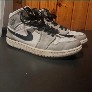 Nike Air Jordans Mid  i grått och svart - Säljer ett par Nike Air Jordans i grått och svart. Skorna har en klassisk design med svart snörning och den ikoniska swoosh-loggan på sidan. Perfekta för både vardag och sportiga tillfällen. Bra skick..