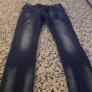 Blå jeans med slitningar - Säljer ett par blå jeans i bra skick med coola slitningar på framsidan. De har en klassisk femficksdesign och en dragkedja. Perfekta för en avslappnad stil och passar till både vardag och fest. Sköna och stiliga!