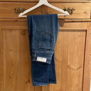 Blå jeans från Replay - Säljer ett par snygga blå jeans från Replay. De har en klassisk femficksdesign med en knapp och dragkedja framtill. Jeansen har en lätt tvättad look som ger dem en cool och avslappnad stil. Perfekta för både vardag och fest storlek w26 L30 