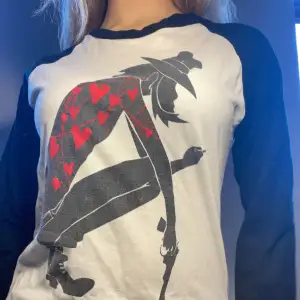 Säljer en cool vit och svart långärmad t-shirt med ett unikt tryck av en figur med röda hjärtan. Perfekt för en avslappnad stil och passar bra till jeans eller kjol. T-shirten är i bra skick och har en normal passform.