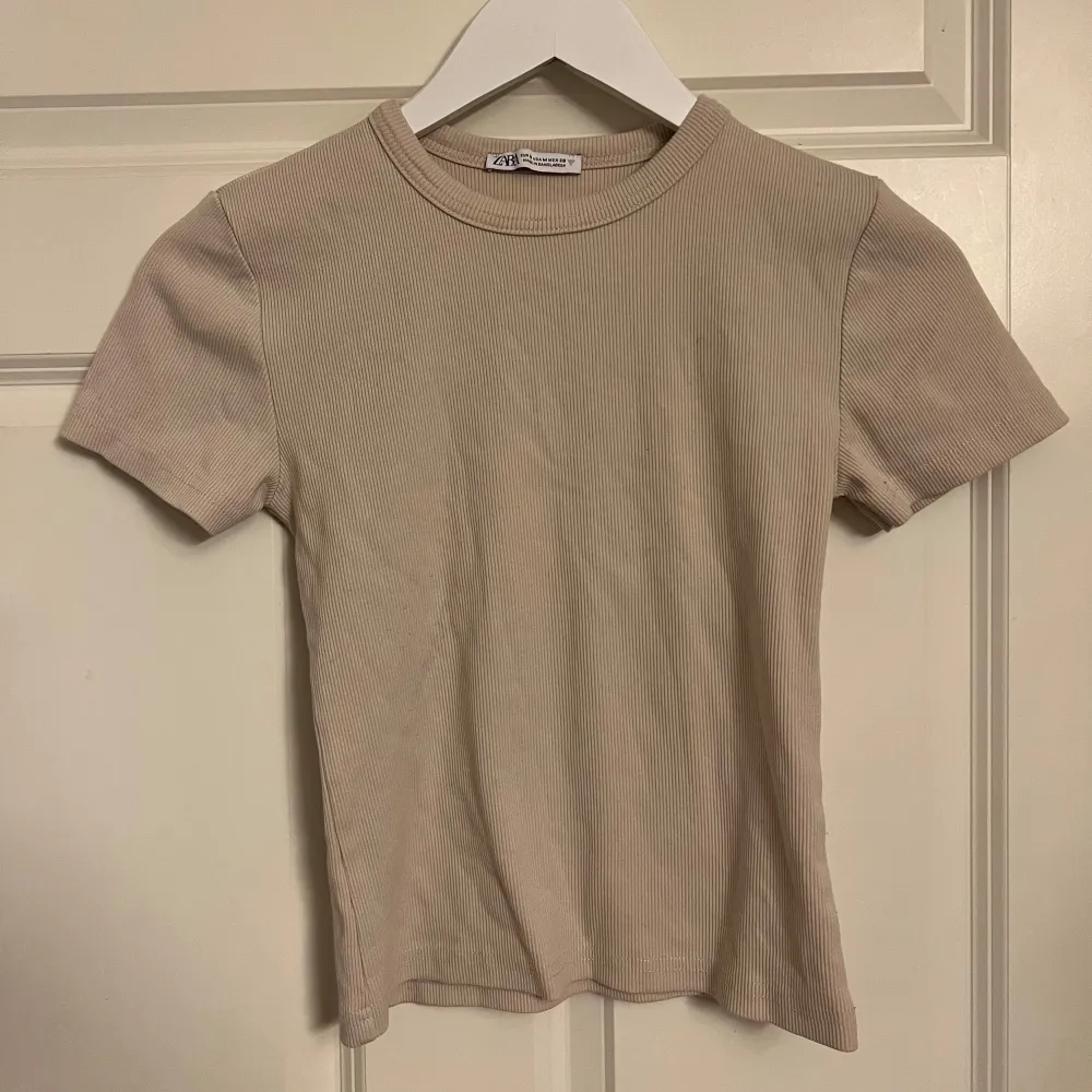 Säljer en superfin beige ribbad T-shirt från Zara i storlek XS. Den har en tight passform och korta ärmar. Toppar.