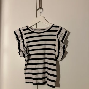 Randig topp med volangärmar - Säljer en superfin randig topp i svart och vitt. Den har korta volangärmar som ger en söt touch. Perfekt för både vardag och fest! 🖤🤍