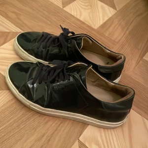 Skor Axel Arigato - Säljer ett par marinblåa sneakers från Axel Arigato i använt skick. De har en glansig yta, storlek står ej men ca 38💙