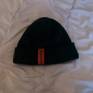 Svart mössa med Jägermeister-logga - Säljer en svart mössa med en cool Jägermeister-logga i orange framtill. Perfekt för att hålla sig varm och stilren under kyliga dagar. Passar både till vardags och festliga tillfällen men främst afterski. Säljer i nyskick då den ej passar mitt huvud. Pris går att diskutera vid smidig affär.