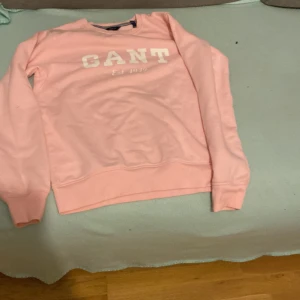 Rosa sweatshirt från GANT - Säljer en superfin rosa sweatshirt från GANT i storlek 170 cm. Den har ett tryck med 'GANT Est. 1949' på framsidan. Perfekt för en avslappnad stil och passar bra till både jeans och kjol. Tröjan är i bra skick och redo för en ny ägare!