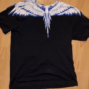 Svart t-shirt med vingmönster från Marcelo burlon Burlon - Säljer en svart t-shirt från Marcelo Burlon i storlek xs. Perfekt för en unik och stilren look. T-shirten är i bomull och har korta ärmar. Storleken är xs men jag skulle säga att den passar small och medium då den är rätt stor. 