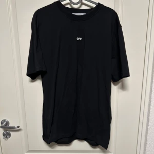  Off-White T-shirt - Säljer en svart t-shirt från Off-White i storlek L. Den har en liten 'OFF' text på framsidan och ett stort grafiskt tryck med månar och pilar på baksidan. Perfekt för en casual look eller streetwear-stil. T-shirten är i bra skick och gjord av mjuk bomull.