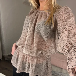Ljusrosa prickig blus - Säljer en superfin ljusrosa blus med små prickar. Blusen har en luftig passform och volangdetaljer vid midjan. Den har långa ärmar och en bekväm, lös passform. Passar både till vardags och fest.