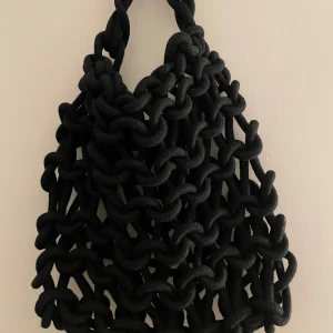 Svart stickad väska - Säljer en unik svart stickad väska med ett coolt, chunky mönster. Perfekt för att ge din outfit en edgy touch. Väskan är handgjord och har en bekväm handtagslängd för att bäras över axeln. Passar perfekt för både vardag och fest!