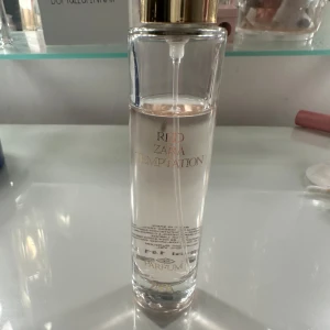 Red Temptation från Zara - Säljer en elegant parfymflaska från Zara, Red Temptation. Flaskan är genomskinlig med en stilren design och har en gyllene kork. Perfekt för den som älskar en sofistikerad och lockande doft. Passar både till vardags och fest!