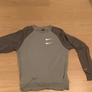 Grå sweatshirt från Nike - Säljer en grå sweatshirt från Nike med vita loggor på bröstet och text på ryggen. Tröjan har långa ärmar i en mörkare grå nyans och är perfekt för både träning och vardag. Den är bra skick och har inga spår för tidigare användning. Skick 9/10.