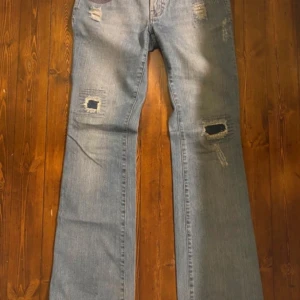 Blå jeans med slitningar - Säljer ett par snygga blå jeans med coola slitningar. De har en bootcut-stil och är perfekta för en avslappnad look. Jeansen är i bra skick och har en klassisk femficksdesign. Perfekta för både vardag och fest! Skriv för mer information