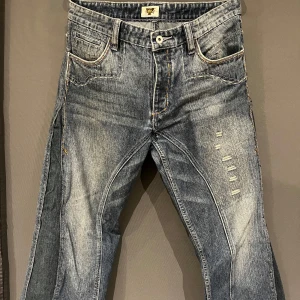 Antik Denim jeans med broderade fickor - Säljer ett par coola Antik Denim jeans i blått med unika broderade detaljer på bakfickorna. Jeansen har en sliten look med fransade benslut och är tillverkade i 100% bomull. 