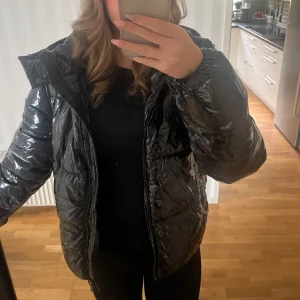 Svart glansig pufferjacka - Säljer en svart glansig pufferjacka i mycket bra skick. Då jag inte använt den. Jackan är fodrad inuti därför väldigt varm! Säljer den eftersom jag köpt en ny vinter jacka!