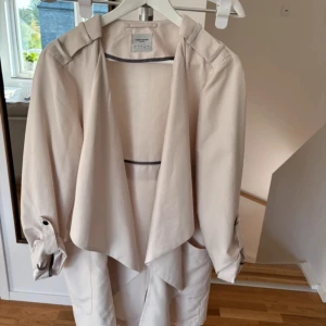 Beige trenchcoat från Veromoda  - Säljer en stilren beige trenchcoat från Vero Moda Jackan har en avslappnad passform med långa ärmar och knappar vid ärmsluten. Perfekt för vår och höst! 🧥