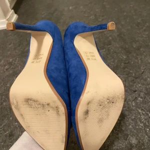 Blå mocka pumps - Snygga blå pumps i mocka med spetsig tå och hög klack. Perfekta för en utekväll eller fest. De har en elegant design som verkligen sticker ut. Använda men i bra skick, med lite slitage på sulorna.