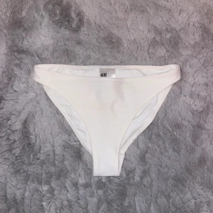 Vit bikiniunderdel  - Säljer en vit bikiniunderdel från H&M i storlek 34. Den är i ribbat material och har en klassisk passform. Perfekt för sommarens stranddagar! Som ni ser på sista bilden finns en liten färgning, men den är på insidan så inget som syns utåt.