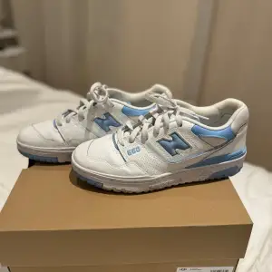 Säljer ett par snygga New Balance 550 sneakers i vitt och blått. De har en klassisk design med snörning och är perfekta för både vardag och träning. Skorna är i mycket bra skick och kommer i originalkartong. Perfekta för dig som vill ha stil och komfort i ett!